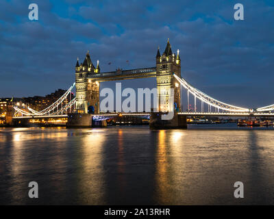 Tower Bridge in der Nacht von Scheinwerfern angestrahlt. Berühmte Tower Bridge am Abend mit blauem Himmel und Reflex auf Wasser, London, England. Nacht citysca Stockfoto