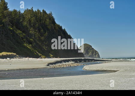 Arizona Beach State Natural Area. Ein Strom fließt über den Strand, unter Felsen, mit Blick aufs Meer spires sichtbar, in der Nähe von Gold Beach, Oregon Stockfoto