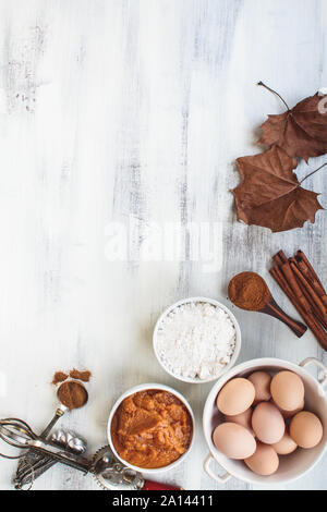 Bestandteile von kürbispüree, Mehl, Zimt und braune Eier mit getrockneten Blätter im Herbst über ein Licht im Hintergrund. Kürbis Brot oder Muffin Rezept. Stockfoto