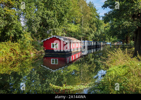 Red Hausboot fest vertäut am Ufer der Basingstoke Canal im Woodham Bereich der Woking, Surrey, Südosten, England, Grossbritannien Stockfoto