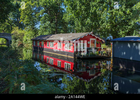 Red Hausboot fest vertäut am Ufer der Basingstoke Canal im Woodham Bereich der Woking, Surrey, Südosten, England, Grossbritannien Stockfoto