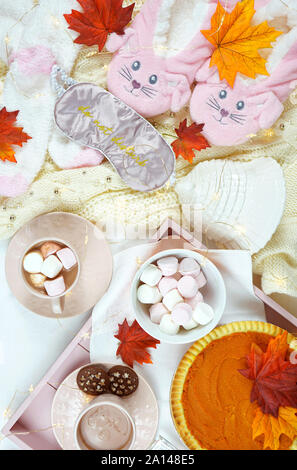 Gemütliche Herbst Thanksgiving im Bett flatlay Overhead mit gemütlichen Pullover, Hausschuhe, Socken und Fach mit Pumpkin Pie und heiße Schokolade mit Marshmallows. Stockfoto