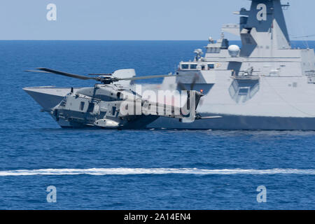 Italienische Marine SH-90 im Flug in der Nähe einer Fregatte FREMM. Stockfoto