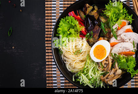 Japanische Ramen-Suppe mit Huhn, Ei, shimeji Champignons und Auberginen auf dunklem Hintergrund. Chanko Nabe, Sumo Suppe. Ansicht von oben Stockfoto