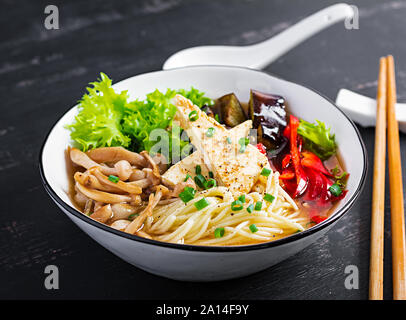 Asiatische vegan Nudeln Suppe mit Tofu Käse, shimeji Pilze und gebratenen Auberginen in Schüssel auf dunklem Hintergrund. Stockfoto