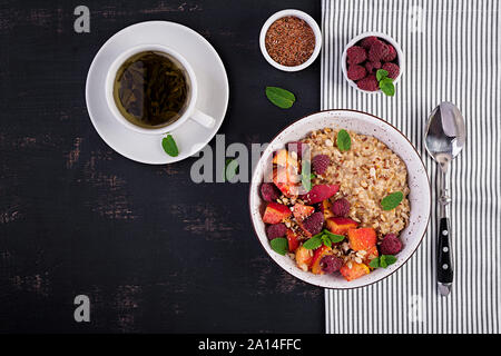 Haferflocken Porridge mit Himbeere und Pfirsich auf dunklem Hintergrund. Gesundes Frühstück. Vegetarisches Essen. Ansicht von oben Stockfoto