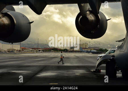 Einen Flieger aus dem 15 Aircraft Maintenance Squadron Spaziergänge auf der Flucht vor einem schweren Regenfälle Joint Base Pearl Harbor-Hickam, New York, Sept. 23, 2019. Der Flieger war Gruß ein C-17 Globemaster III, die gerade von Papua Neuguinea zurückgekehrt war mit Mitarbeitern aus der Verteidigung POW/MIA Accounting Agentur (DPAA). Die Mannschaft kam mit möglich bleibt der Service Mitglieder während des Zweiten Weltkriegs verloren. DPAA's Mission ist es, die möglichst vollständige Buchhaltung unserer fehlt Personal zu ihren Familien und der Nation zu stellen. (U.S. Air Force Foto: Staff Sgt. Apryl Hall) Stockfoto