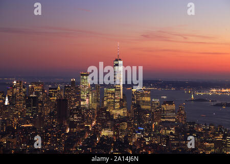Luftaufnahme von New York City, Manhattan Skyline leuchtet bei Sonnenuntergang einschließlich das One World Trade Center und Liberty Island, USA Stockfoto