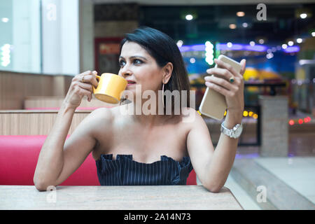 Stilvolle Junge Frau trinkt Kaffee und mit Ihrem Mobiltelefon im Cafe Stockfoto