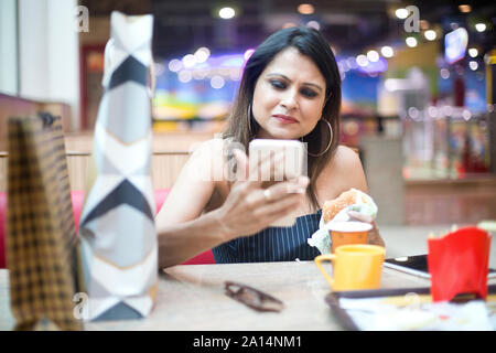 Modische Frau trinkt Kaffee und Burger essen nach dem Shopping in modernen Mall Stockfoto
