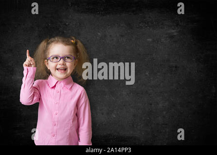 Smilling kid Erfinder mit rised Hand denken und die Suche nach Idee, in der Nähe der Schule schwarz Schwarzes Brett Stockfoto