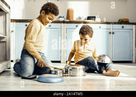 Zwei Jungs sitzen auf dem Boden der Küche und spielt mit den Pfannen. Stockfoto