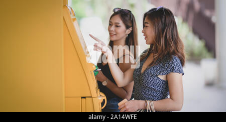 Zwei schöne asiatische Frauen ziehen das Geld von einer Bank mit Geldautomat in der Mall Stockfoto