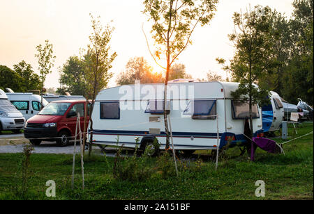 Wohnwagen und Wohnmobile auf der grünen Wiese in einem Campingplatz. Sunrise, Strahlen auf Camper in den Morgen. Grüne Gras. Outdoor Konzept für Reisen und res in der n Stockfoto