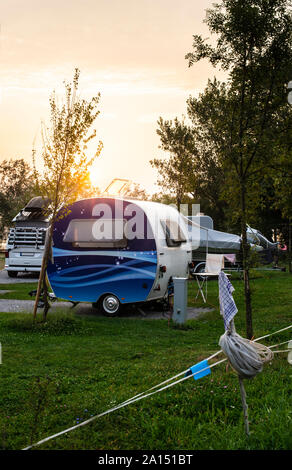 Wohnwagen und Wohnmobile auf der grünen Wiese in einem Campingplatz. Sunrise, Strahlen auf Camper in den Morgen. Grüne Gras. Outdoor Konzept für Reisen und res in der n Stockfoto