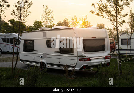 Wohnwagen und Wohnmobile auf der grünen Wiese in einem Campingplatz. Sunrise, Strahlen auf Camper in den Morgen. Grüne Gras. Outdoor Konzept für Reisen und res in der n Stockfoto