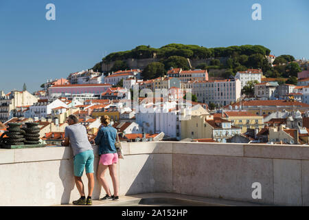 Zwei Touristen am Arco da Rua Augusta (Rua Augusta Arch) Aussichtsplattform mit Sao Jorge und Blick auf die Stadt hinter in Lissabon, Portugal. Stockfoto