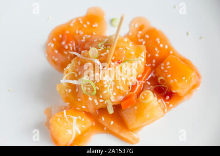 Ein Strahl Wange, die tief in Teig gebacken wurde und serviert mit süß-saurer Sauce und garniert mit fein geschnittenen Frühlingszwiebeln und Sesam. Stockfoto