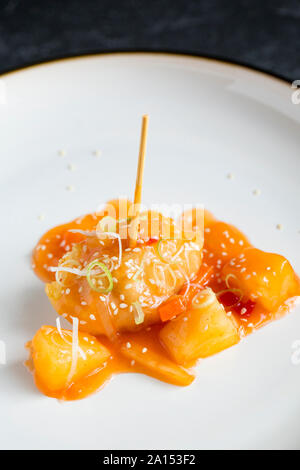 Ein Strahl Wange, die tief in Teig gebacken wurde und serviert mit süß-saurer Sauce und garniert mit fein geschnittenen Frühlingszwiebeln und Sesam. Stockfoto