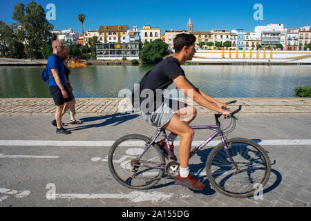 Radfahrer reiten entlang der Ufer des Flusses Guadalquivir. Zurück Vorderansicht von Häusern und Wohnungen im Barrio Triana Viertel von Sevilla - Sevilla Stockfoto