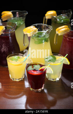 Limonade und Kwass home Vorbereitung. Limonade in die Kanne, und Zitronen mit Minze auf den Tisch indoor. Rosa Limonade mit Zitrone, Limette und Erdbeeren. Stockfoto