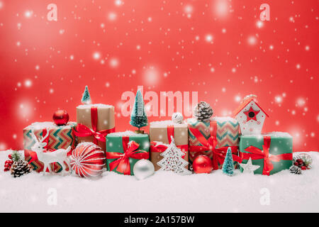 Weihnachtsgeschenke und Ornamente in einer Reihe in der Form eines schneebedeckten Stadtbild mit rotem Hintergrund Stockfoto