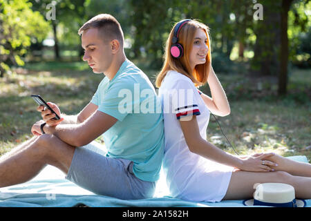 Junge Teenager paar Spaß im Freien im Sommer. Mädchen mit roten Haaren Musik in rosa Ohrhörer und Boy Chat am Telefon verkaufen. Stockfoto