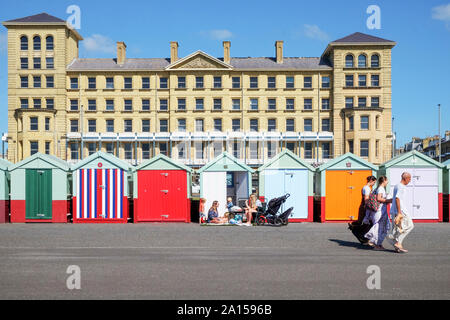 Brighton, East Sussex, Großbritannien, Großbritannien - 13 September, 2019: eine Linie von bunten Badekabinen mit einer Familie sitzt außerhalb einer von ihnen, und drei m Stockfoto