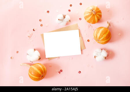 Mockup Postkarte mit craft-Umschlag und kleine Kürbisse, glitter Dekor und Baumwolle Blumen auf rosa Hintergrund. Minimal Style Zusammensetzung Stockfoto