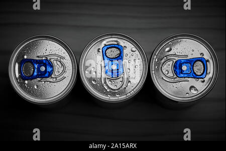 Drei Energy Drink Dosen aus Aluminium mit Wassertropfen, von oben auf dunklem Hintergrund Stockfoto