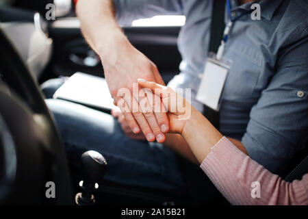 Männliche auto Kursleiter nimmt Untersuchung in der jungen Frau. Die Hände schütteln. Zusammen im Auto sitzen. Tageslicht draußen. Vereinbarung. Bestehen der Prüfung Stockfoto