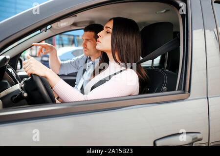Männliche auto Kursleiter nimmt Untersuchung in der jungen Frau. Kerl helfen Studentin Auto zu fahren. Consulting. Zusammen sitzen. Das Bestehen der Prüfung. Tageslicht außerhalb Stockfoto