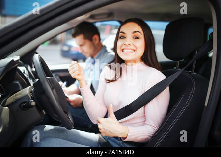Männliche auto Kursleiter nimmt Untersuchung in der jungen Frau. Gerne positives Modell sehen Sie auf Kamera mit Daumen nach oben. Lächelnd mit Mag. Kursleiter neben ihr sitzen. Stockfoto