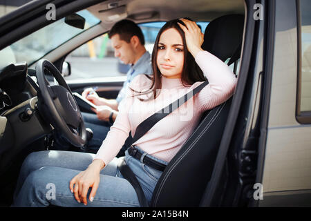 Männliche auto Kursleiter nimmt Untersuchung in der jungen Frau. Langeweile Frau Blick auf Kamera und Pose. Zusammen im Auto sitzen. Prüfung bestanden. Tageslicht Stockfoto