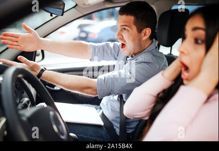 Männliche auto Kursleiter nimmt Untersuchung in der jungen Frau. Stress während der Fahrt. Angst junge Frau den Kopf mit den Händen berühren. Hinweis für den Kursleiter, die schreien und Stockfoto