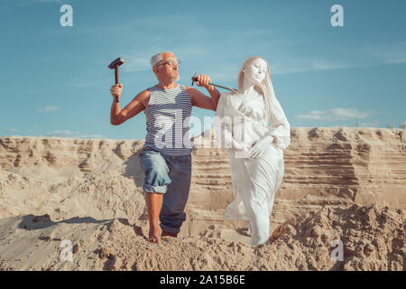 Ein alter Mann macht die Statue einer Frau aus Stein. In seinen Händen ist ein Werkzeug zum Erstellen von Frauen. Ein Mann schafft eine Frau. Stockfoto