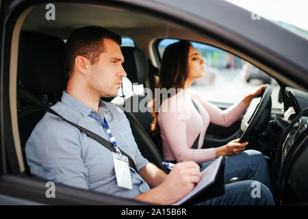 Männliche auto Kursleiter nimmt Untersuchung in der jungen Frau. Vorsicht Lehrer freuen. Schüler fahren Auto. Ernst und konzentriert Stockfoto