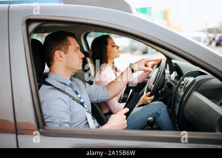 Männliche auto Kursleiter nimmt Untersuchung in der jungen Frau. Vorsichtig fahren und die praktische Prüfung. Kursleiter helfen, mit dem Fahren. Junge Frau Test bestanden mit c Stockfoto