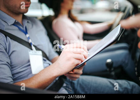 Männliche auto Kursleiter nimmt Untersuchung in der jungen Frau. Nahaufnahme von Mann schreiben auf Papier. Die praktische Prüfung. Junge Frau, die mit Zuversicht Stockfoto