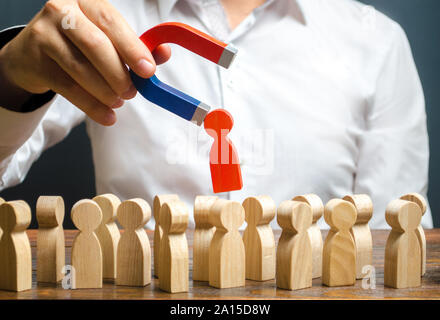 Eine Hand mit einem Magnet zieht Rot menschliche Figur aus der großen Masse der Leute. Die Einstellung neuer Arbeitnehmer, Headhunter. Suche nach begabten Mitarbeiter. Nachfrage fo Stockfoto