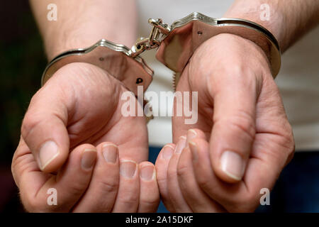 Männer die Hände in den Handschellen. Ein Mann in einem weißen T-Shirt in Handschellen. Close-up Stockfoto