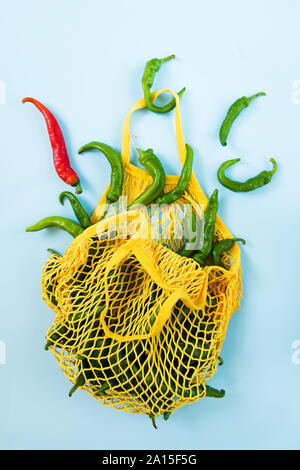 Kreative Gestaltung grüne Chilischoten in Gelb string Beutel auf Pastell-blaue Hintergrund. Haufen grüne Paprika namens frigitelli in Italien, Null Abfall, Stockfoto