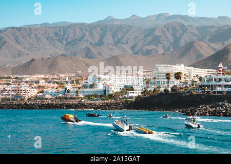 Teneriffa, Spanien - August 2019: Motorboote am Ozean Küste mit Hotels, die Stadt und die Berge im Hintergrund an der Costa Adeje auf Teneriffa Stockfoto