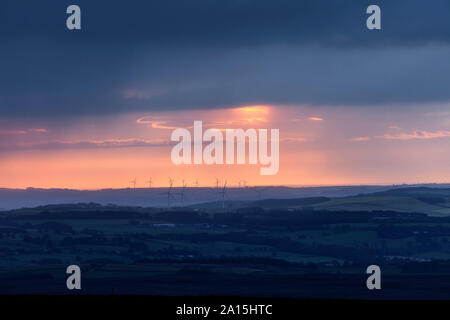 Ferner Windenergieanlagen unter einem dramatischen Himmel bei Sonnenaufgang, gesehen von der North Pennines in der Grafschaft Durham, Großbritannien Stockfoto