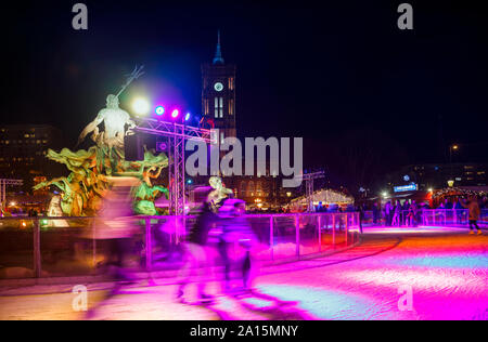 Berlin, Deutschland - 12 Dezember, 2018: Leute Eislaufen am Eislaufplatz am Weihnachtsmarkt in Berlin Mitte in der Nacht. Skater sind verschwommen in Bewegung. Rotes Rathaus (R Stockfoto