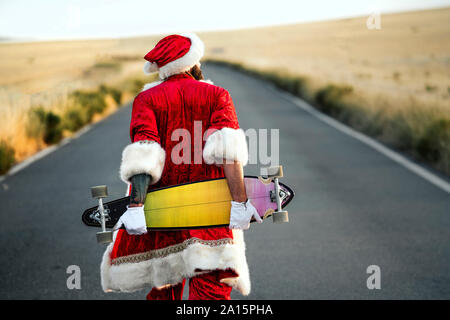 Ansicht der Rückseite des Santa Claus mit einem Longboard auf Landstraße Stockfoto