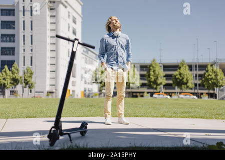 Lächelnden jungen Mann neben e-Scooter in der Stadt Stockfoto