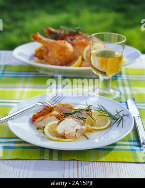 Gebratenes Huhn in Zitronensauce und Glas Weisswein auf Garten Tisch Stockfoto