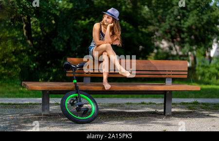 Junge Frau mit Einrad sitzen auf einer Parkbank Stockfoto