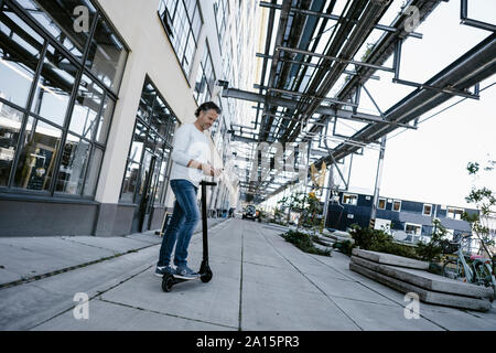 Reifer Mann mit Smartphone und Elektroroller Stockfoto